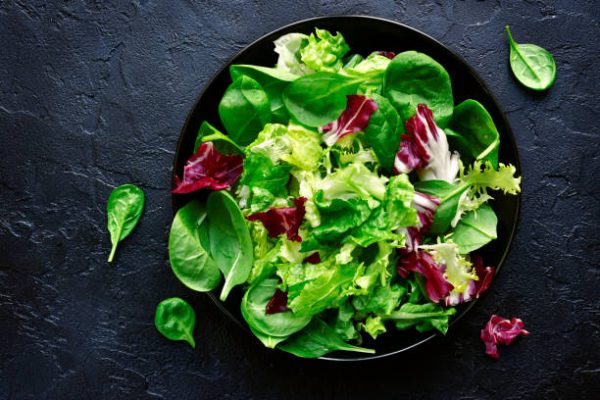 Mix salad leaves in a black bowl over dark slate, stone or concrete background.Top view with copy space.