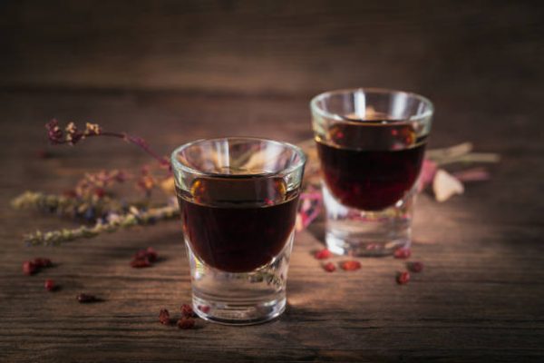 Two glasses of alcoholic drink on dark wooden background. Herbal bitter liqueur with different natural ingredients.